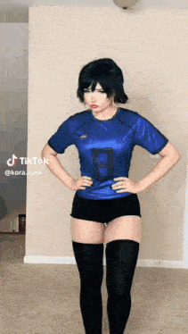 a girl in a blue shirt and black shorts is standing with her hands on her hips .