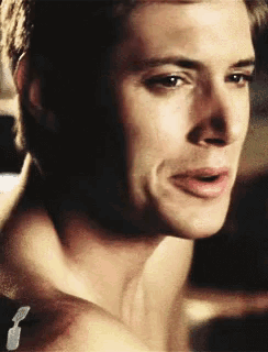 a close up of a man 's face with his mouth open and a tattoo on his shoulder .