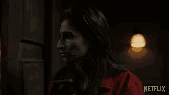 a woman in a red jacket is standing in a dark room with a netflix logo in the corner