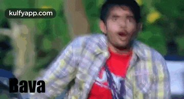 a man in a plaid shirt and a red shirt is making a funny face while sitting on a bench .