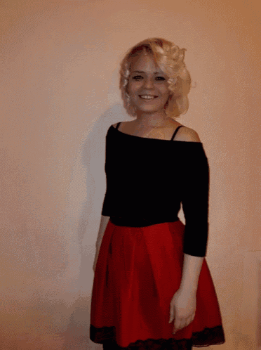 a woman wearing a black off the shoulder top and a red skirt smiles