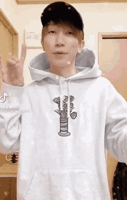 a man wearing a white hoodie and a black hat is giving a peace sign