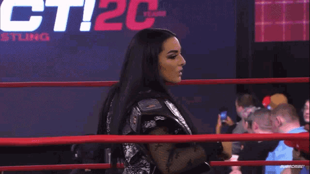 a woman stands in a wrestling ring with a sign behind her that says ' tic ' on it