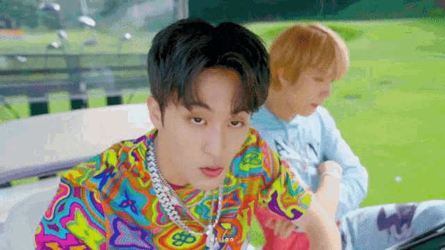 two young men are sitting in a golf cart on a golf course . one of the men is wearing a colorful shirt .