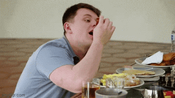 a man is sitting at a table with plates of food and a bottle of water .