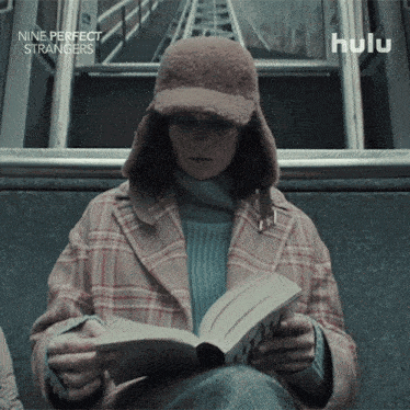 a woman is reading a book while wearing a hat with the words nine perfect strangers below her