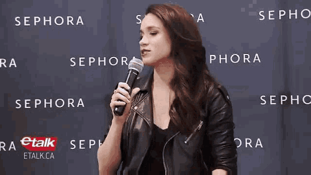 a woman in a leather jacket holds a microphone in front of a sephora sign