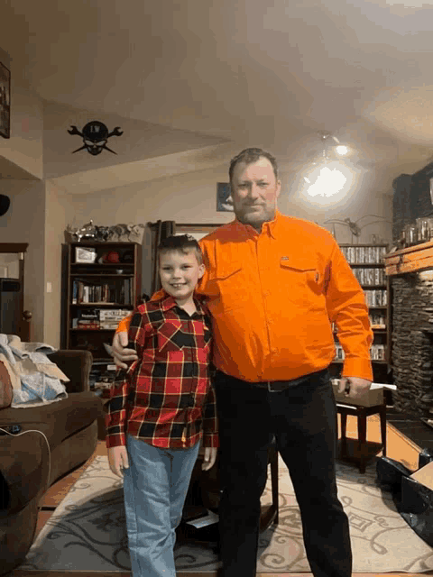 a man in an orange shirt stands with a boy in a plaid shirt
