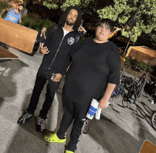 two men are standing next to each other in a parking lot . one of the men is holding a bottle of water .