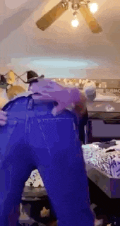 a person in blue jeans is standing in a room with a ceiling fan in the background .