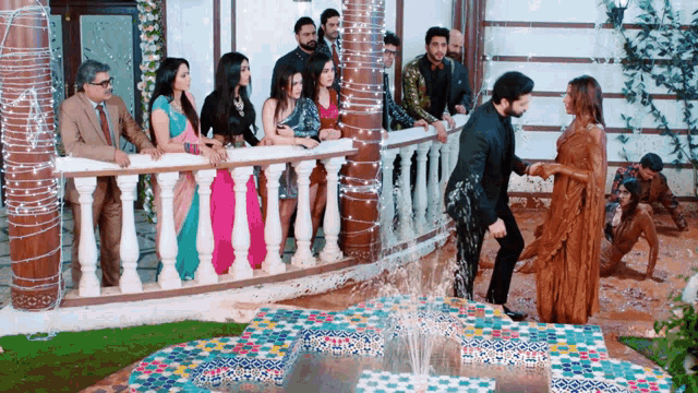 a group of people are standing around a fountain while a man stands next to a woman .