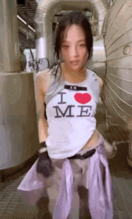 a woman wearing a white tank top that says `` i love me '' is standing in front of a building .