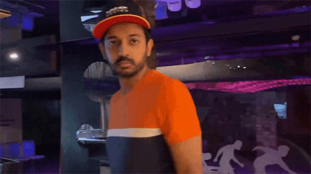 a man wearing an orange shirt and a red hat stands in a room