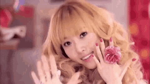 a young woman with blonde hair and red nails is smiling and waving .