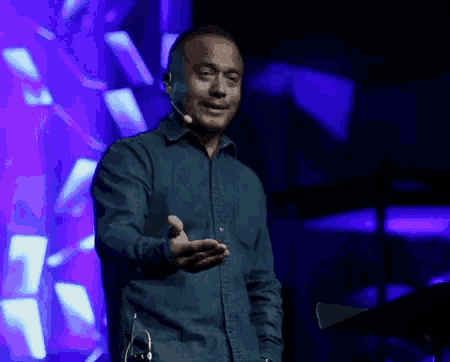 a man in a blue shirt is standing on a stage with a microphone .