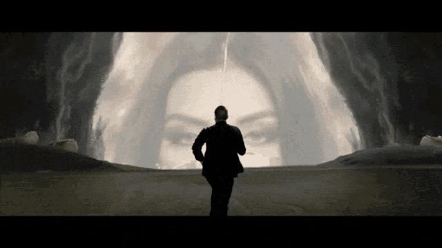 a man in a suit is standing in front of a large painting of a woman