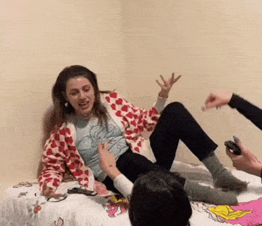 a woman is sitting on a bed with her legs crossed while a man holds a cell phone .