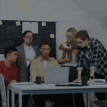 a group of people are gathered around a table looking at a laptop