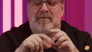 a man with glasses and a beard is holding something in his hands and making a heart shape with his hands .