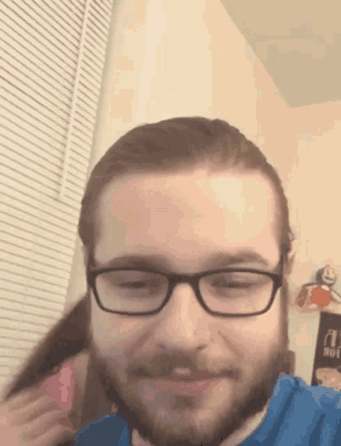 a man with glasses and a beard is smiling while a woman holds his hair .