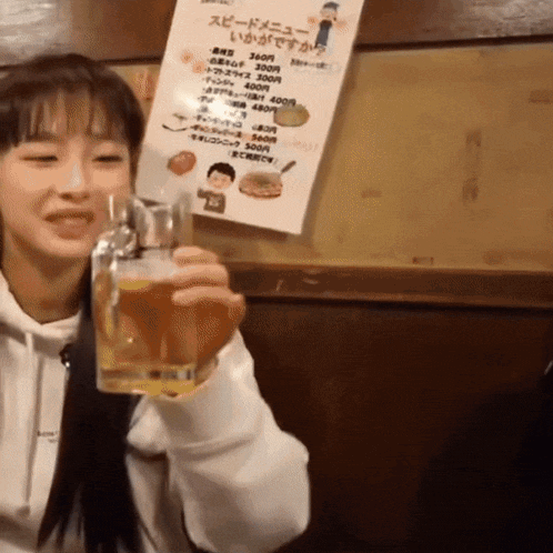 a woman holds a glass of beer in front of a menu in a foreign language