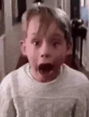 a young boy with his mouth open is wearing a white sweater .