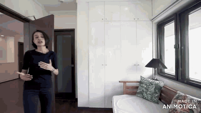 a woman in a black shirt is standing in a room with a couch and a lamp made in animotica