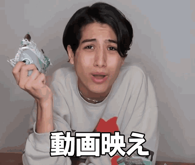 a man in a white sweatshirt holds something in his hand with chinese writing on the bottom right