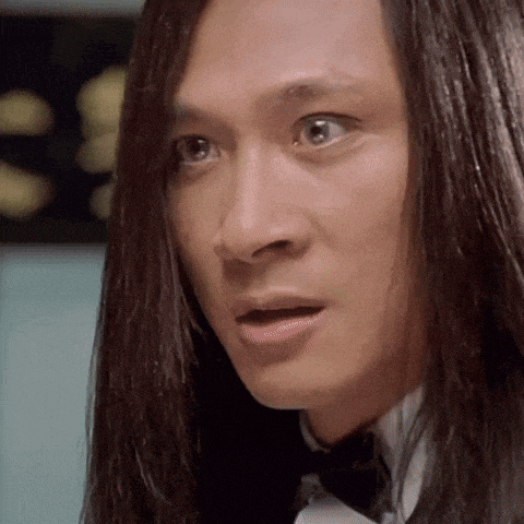 a man with long hair is wearing a tuxedo and bow tie and making a surprised face .
