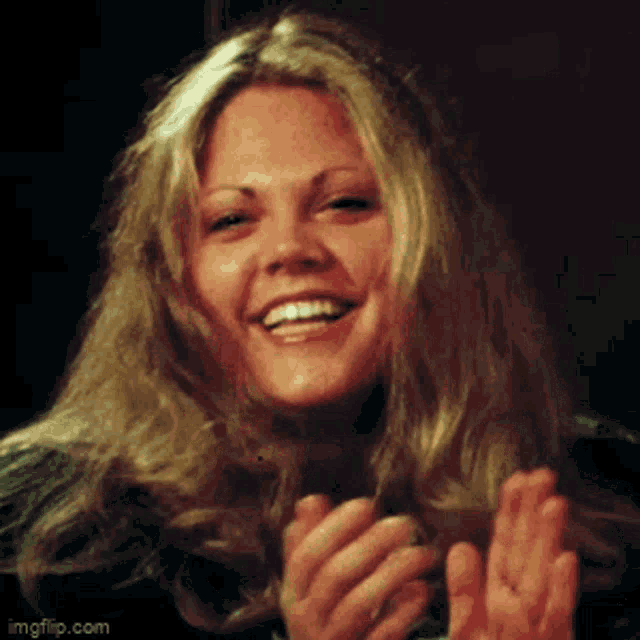 a woman with blonde hair is smiling and clapping her hands .
