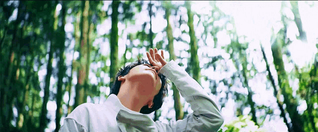 a man in a white shirt is standing in the woods looking up at the sky .