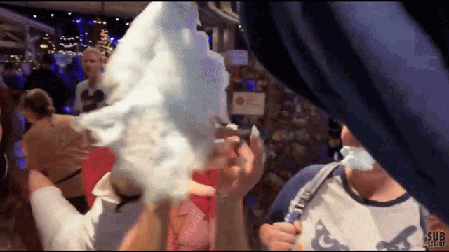 a person eating cotton candy in a crowd with the words sub scribe visible in the corner