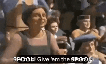 a woman is standing in front of a crowd of people and saying `` spoon ! give ' em the spoon '' .
