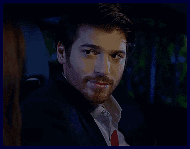 a man with a beard wearing a suit and tie looks at the camera