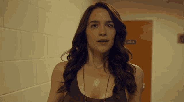 a woman in a burgundy tank top stands in a hallway in front of a sign that says ' locker room '