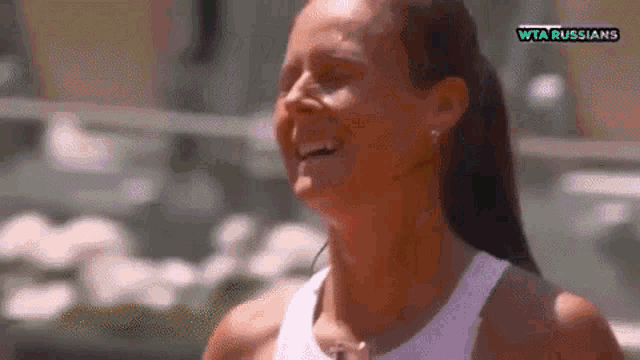 a woman in a white tank top is laughing in front of a screen that says wta russians .