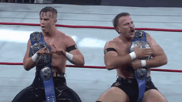 two wrestlers in a ring with blue belts on