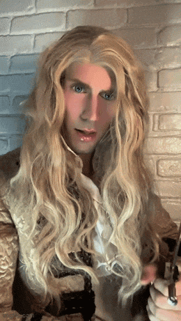 a man with long blonde hair and blue eyes holds a key