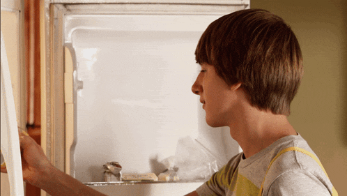a young man is looking into an empty refrigerator door