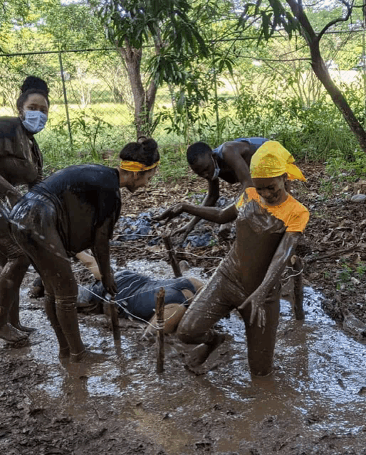a group of people are playing in the mud with one wearing a yellow shirt