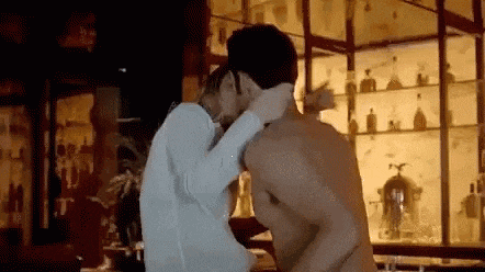 a man and a woman are kissing in a bar . the man is shirtless and the woman is wearing a white shirt .