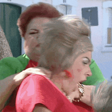 a woman in a green jacket is hugging another woman in a pink dress