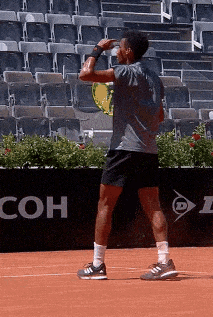 a man stands on a tennis court with a sign that says coh on it