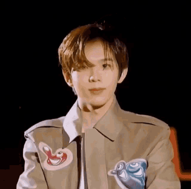 a close up of a young man wearing a tan jacket with a penguin on the sleeve .