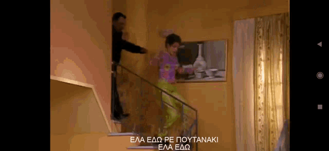 a woman in a pink top and green pants is walking down a set of stairs while a man stands behind her