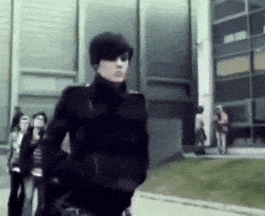 a man in a black jacket is walking in front of a building