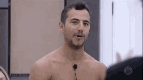 a shirtless man with a microphone in his ear is talking to another man .