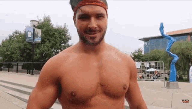 a shirtless man with a red headband on his head is standing in front of a building .