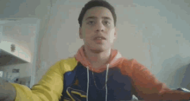 a man wearing a colorful hoodie is standing in front of a wall .
