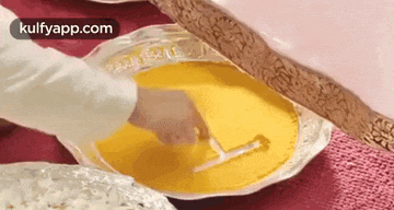 a person is stirring a yellow liquid in a bowl with a spoon .